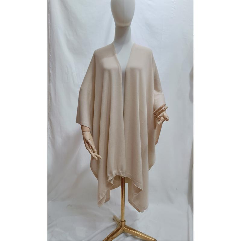 Beżowe ponczo cape oversize z dzianiny, zapięcie open-front, drapowane na manekinie, miękki neutralny ton, prążkowany brzeg.