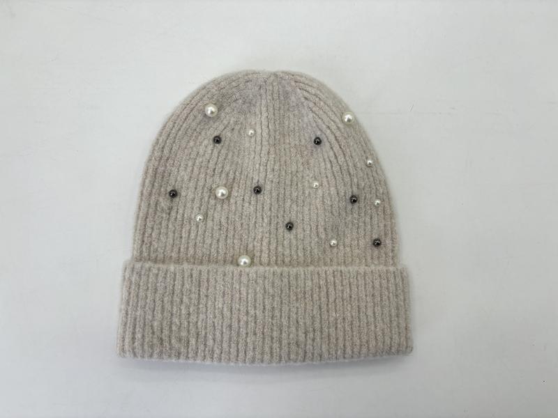 Beżowa prążkowana czapka beanie zdobiona białymi perłami i ciemnymi kryształkami, na białym tle.