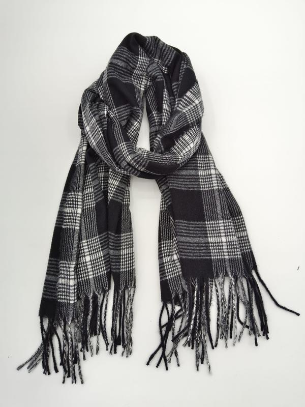 Czarno-biały szalik w kratę tartan z frędzlami, luźno zawiązany, na białym tle.