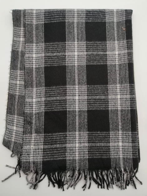 Złożony koc w czarno-białą kratę tartan z frędzlami na węzełkach, na białym tle.