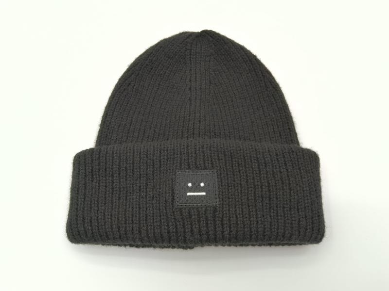 Czarna gruba czapka beanie z prążkowanego dzianiny ze zwiniętym mankietem i naszytą łatką z neutralną twarzą.