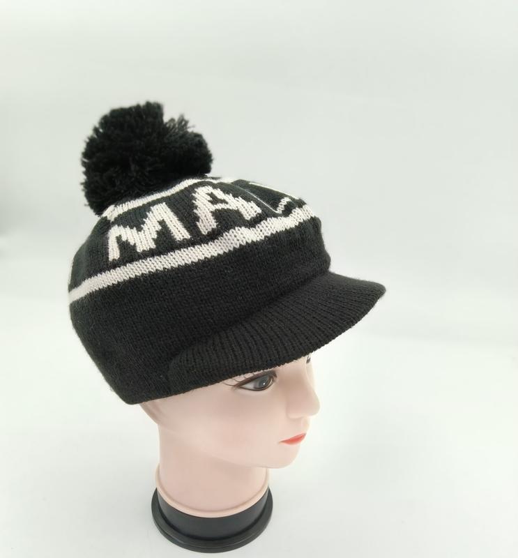 Czarna czapka beanie z daszkiem, pomponem i białym wzorem literowym.