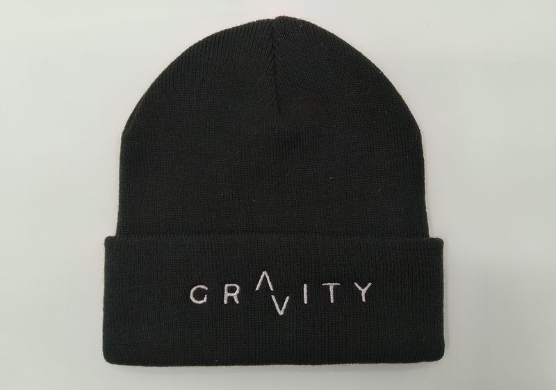 Czarna prążkowana czapka beanie z podwiniętym mankietem i białym haftowanym logo GRAVITY, na białym tle.