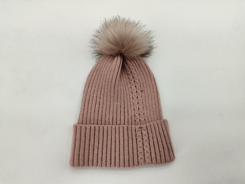 Różowa prążkowana czapka zimowa beanie z dużym pomponem ze sztucznego futra na białym tle.