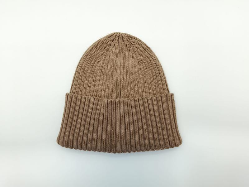 Beżowa czapka beanie z grubym prążkowanym splotem i mankietem, widok z góry na białym tle.