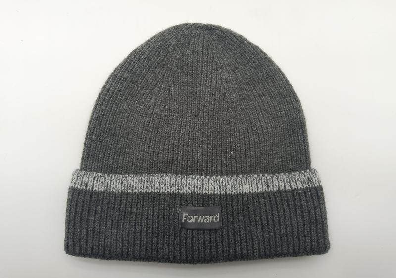 Ciemnoszara prążkowana czapka beanie z jasnoszarym paskiem na wywiniętym mankiecie i małą naszywką, na białym tle.