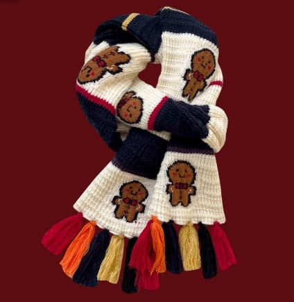 Kremowo-granatowy szalik chunky knit ze wzorem pierniczków i kolorowymi frędzlami na bordowym tle.