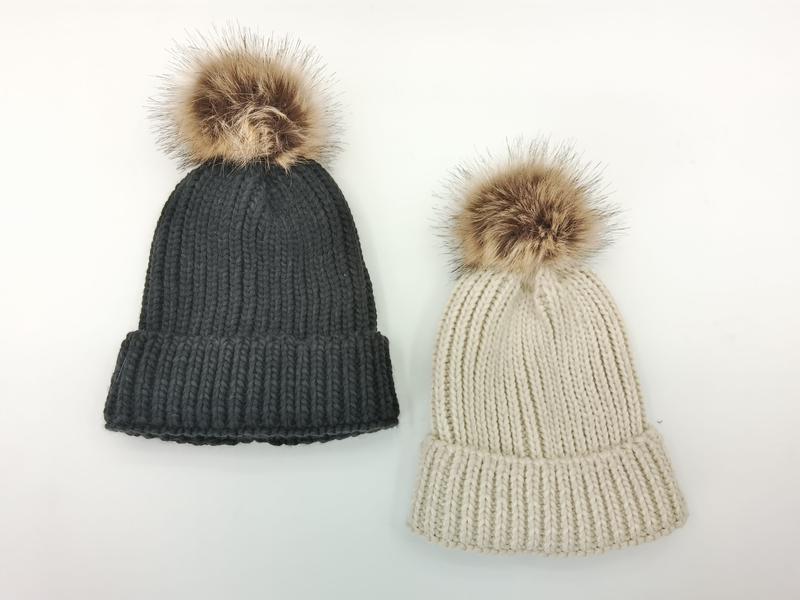Dwie czapki beanie z grubym prążkowanym splotem i pomponem ze sztucznego futra w kolorze antracytowym i beżowym.