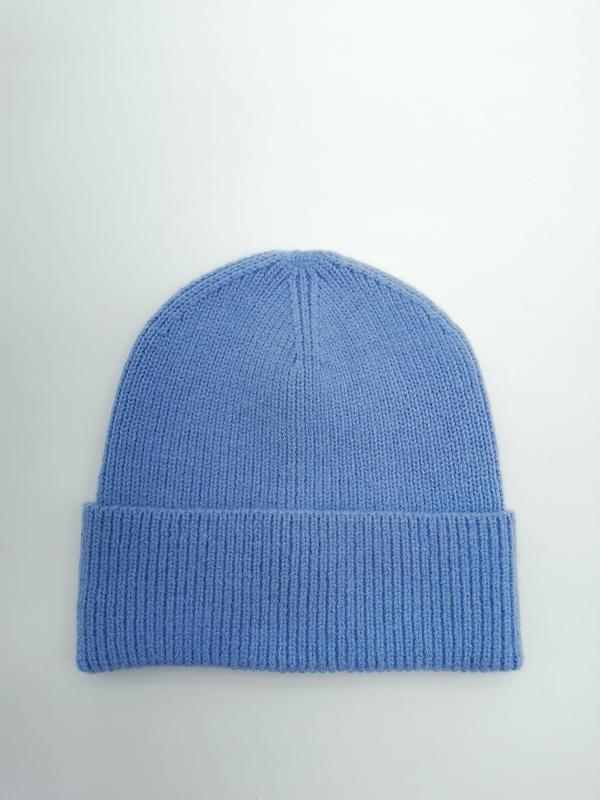 Chabrowa czapka beanie z dzianiny z podwiniętym ściągaczem na jasnoszarym tle.