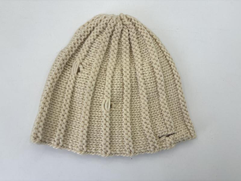 Kremowa czapka beanie z grubego ryżowego splotu w kolorze kości słoniowej, złożona prezentując fakturę dzianiny.