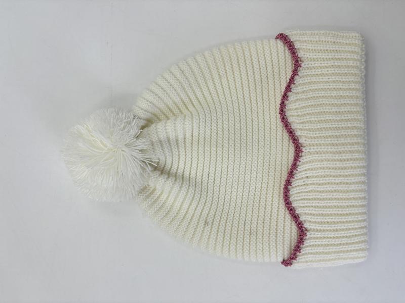 Kremowa czapka beanie z grubego dzianiny z puszystym pomponem i różowym zdobieniem w zygzak przy brzegu.