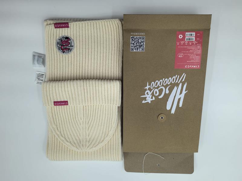 Kremowy prążkowany komplet: czapka beanie i szalik z bordowym logo, obok pudełka prezentowego kraft.