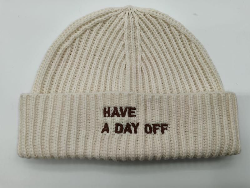 Kremowa czapka beanie z grubym prążkowanym splotem i brązowym haftem 'Have A Day Off' na mankiecie.