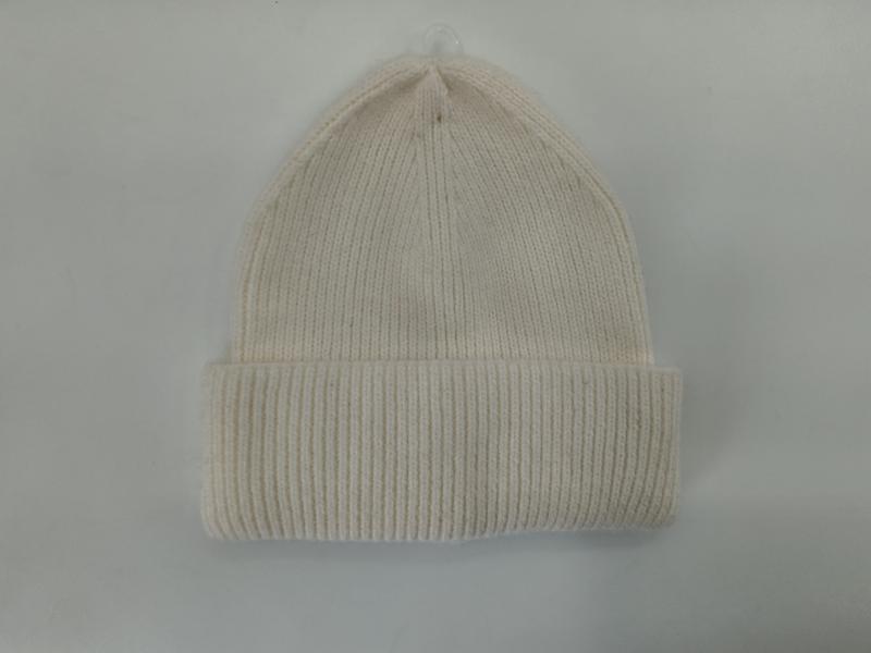 Kremowa czapka beanie z prążkowanej dzianiny z podwiniętym mankietem, prezentowana na jasnoszarym tle.