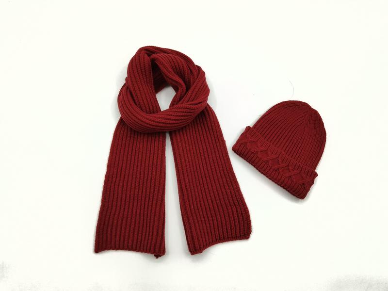 Ciemnoczerwony szalik z prążkowanej dzianiny obok dopasowanej czapki beanie na białym tle.