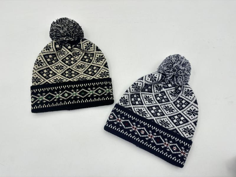 Dwie czapki beanie Fair Isle z pomponem w czarno-kremowym i granatowo-białym wzorze nordyckim na białym tle.