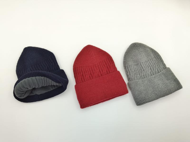 Trzy czapki beanie z dzianiny w prążki w kolorach granatowym, czerwonym i szarym z polarową podszewką na białym tle.