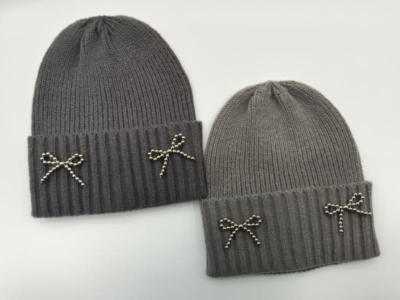 Szara prążkowana czapka beanie z ozdobną kokardką z srebrnych koralików na mankiecie, w kolorze ciemno- i jasnoszarym.