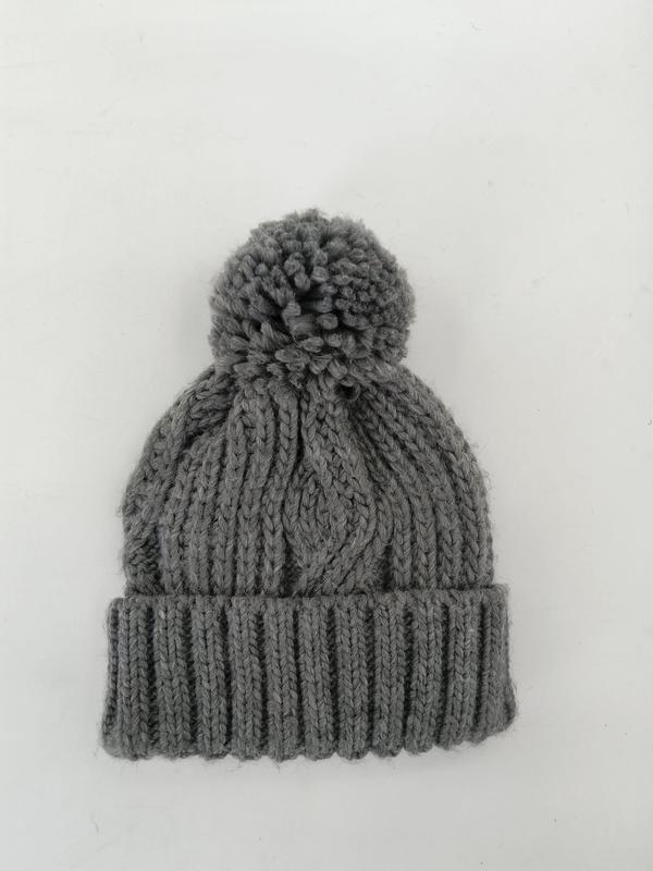 Szara czapka beanie z grubym warkoczowym splotem, dużym pomponem i ściągaczem, widok z góry na białym tle.