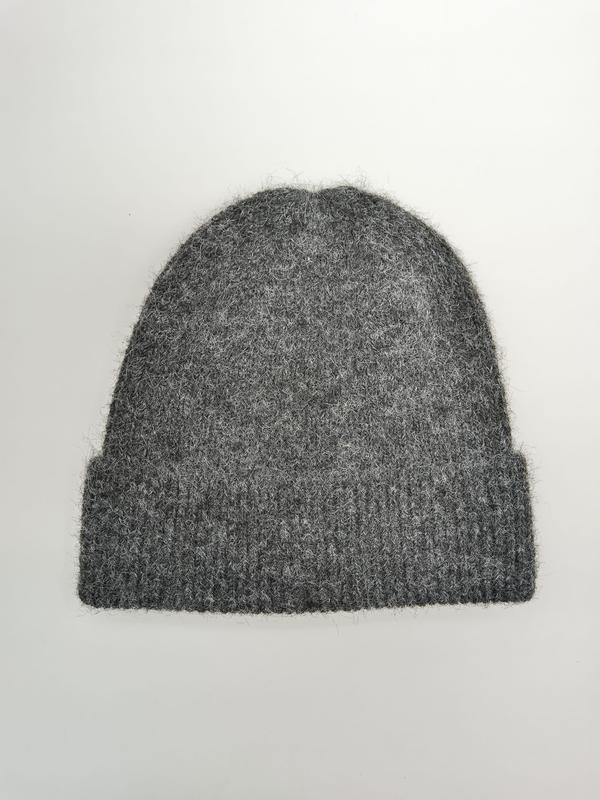 Szara puszysta czapka beanie z dzianiny z prążkowanym mankietem, ułożona płasko na białym tle.