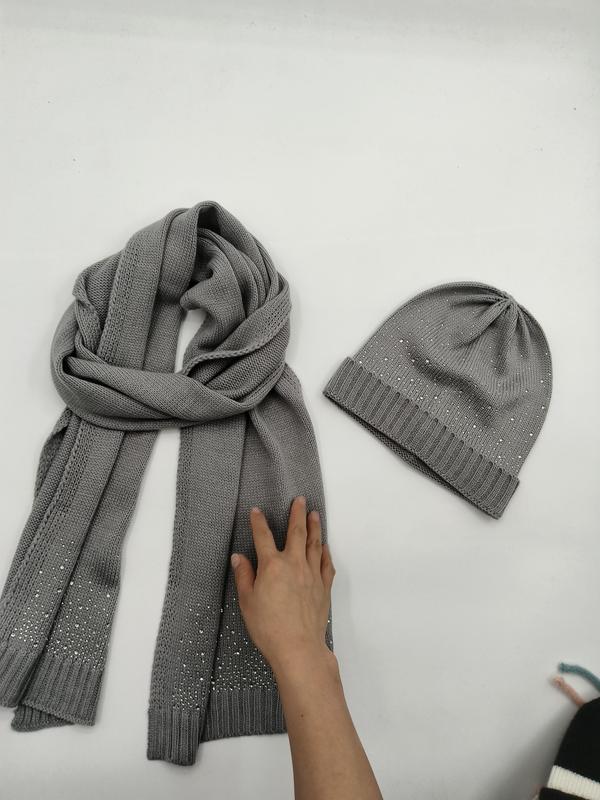 Szary dzianinowy zestaw: szalik i czapka beanie z ozdobami z dżetów, ułożone płasko na białym tle.
