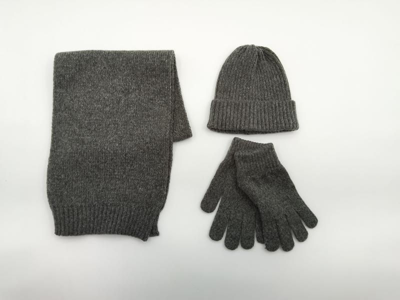 Szary melanżowy komplet zimowy z dzianiny: szalik, czapka beanie w prążki i rękawiczki na białym tle.