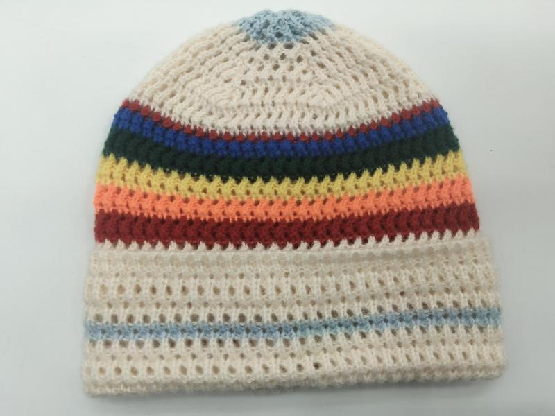 Ręcznie robiona czapka beanie szydełkowa z tęczowymi paskami na kremowym tle, ażurowy splot, widok z góry.