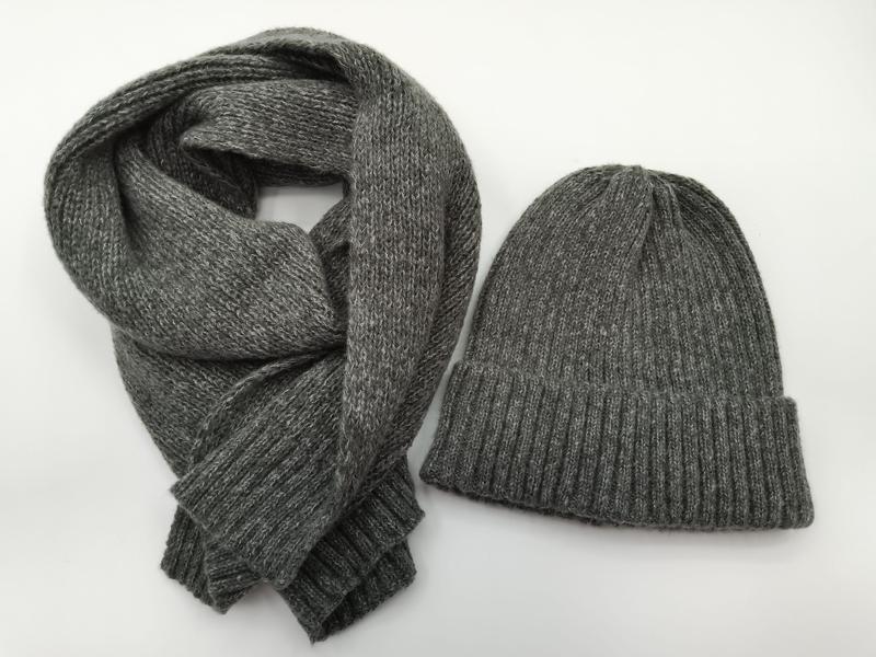 Szara czapka beanie i pasujący szalik z dzianiny w prążki, ułożone na białym tle.