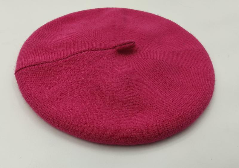 Różowy beret z delikatnej wełny z żebrowanym rondem i centralnym chwostem, widok z góry na białym tle.