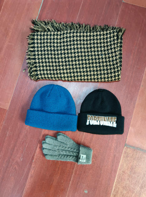 Zestaw zimowy: szalik w pepitkę z frędzlami, niebieska czapka waffle knit, czarna czapka i szare rękawiczki.