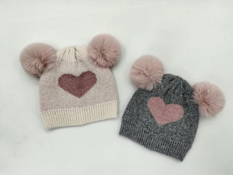 Dwie dziecięce czapki beanie z podwójnymi pomponami ze sztucznego futra i motywem serc – kremowa i szara.