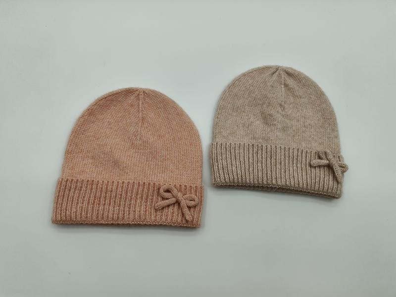 Dwie miękkie czapki beanie z kokardą – różowa i beżowa, żebrowane mankiety, widok z góry.