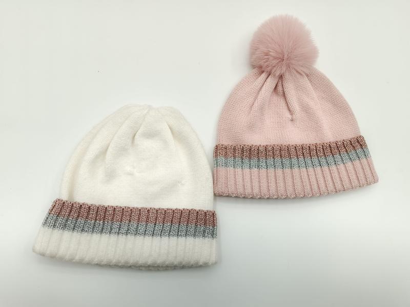 Dwie czapki beanie z dzianiny w kolorze białym i różowym, z metaliczną lamówką, różowa czapka z pomponem z futra.