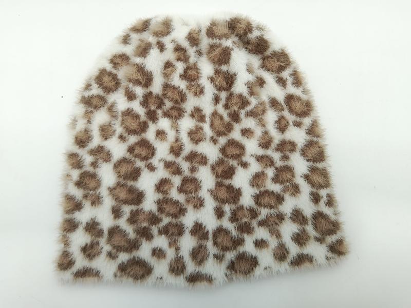 Miękka czapka beanie z białego sztucznego futra z brązowym wzorem w panterkę, na białym tle.
