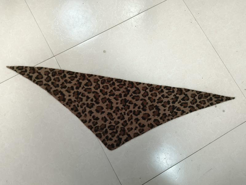 Trójkątna chusta bandana we wzór leoparda z brązowymi i czarnymi cętkami, złożona płasko na białej posadzce.