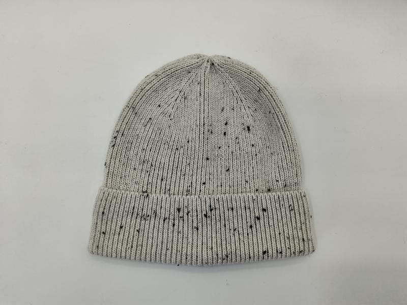 Jasnoszara dzianinowa czapka beanie z czarnymi plamkami i podwiniętym ściągaczem, widok z góry na białym tle.