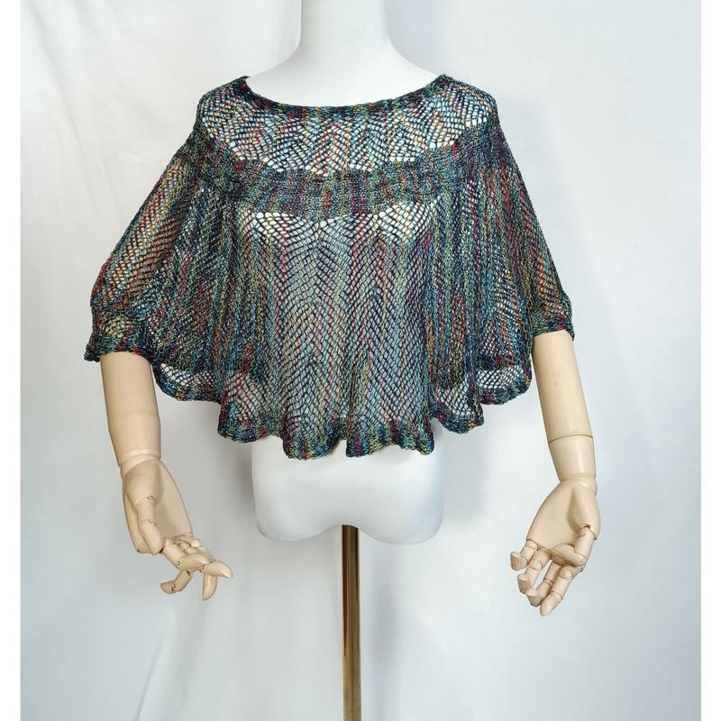 Kolorowe ponczo cape z dzianiny szydełkowej w stylu boho, ażurowy splot, na manekinie z drewnianymi dłońmi.