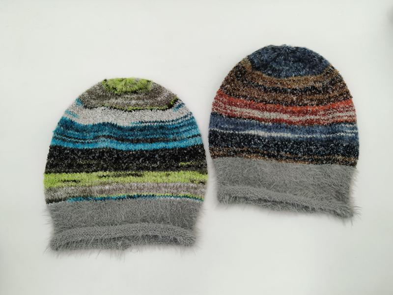 Dwie czapki beanie w kolorowe paski – wariant niebiesko-zielony i czerwono-brązowy, obie z szarym puszystym mankietem.