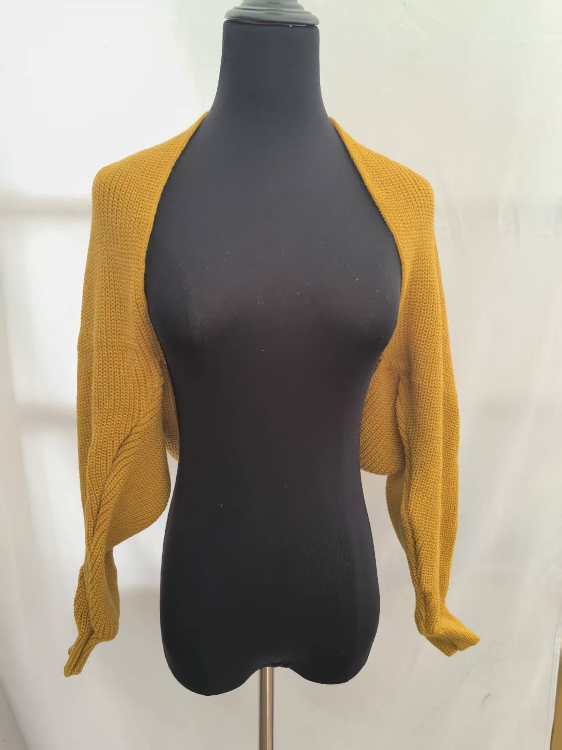 Musztardowy sweter bolero o grubym splocie, skrócony krój, długie rękawy, prezentowany na czarnym manekinie.