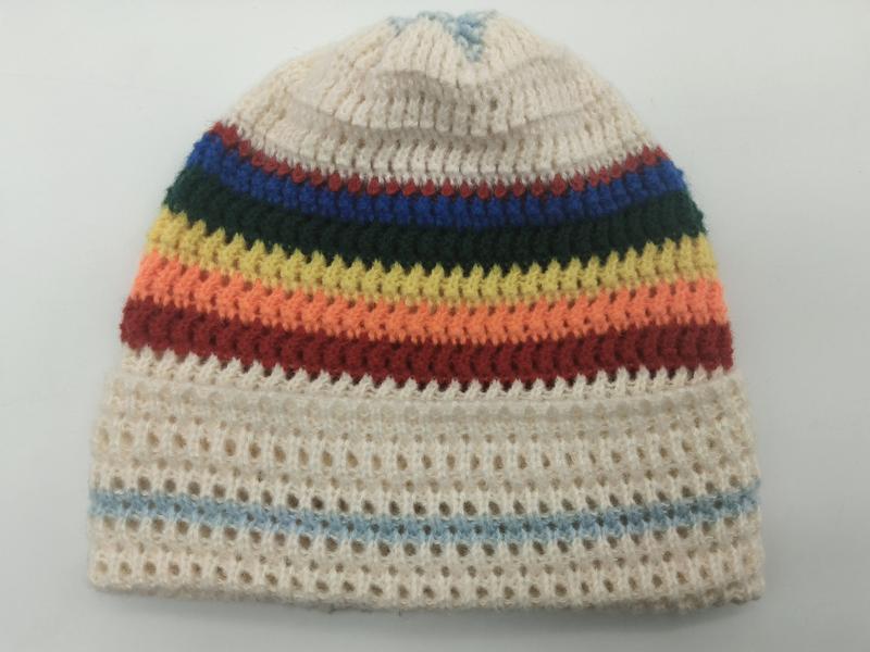Ręcznie dziergana kremowa czapka beanie z tęczowymi paskami w kolorach czerwonym, pomarańczowym, żółtym, zielonym i niebieskim na ażurowej podstawie.