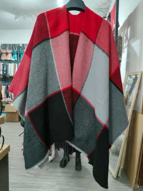 Tkane ponczo cape w geometryczny wzór color block w kolorach czerwonym, szarym i czarnym, na wieszaku.