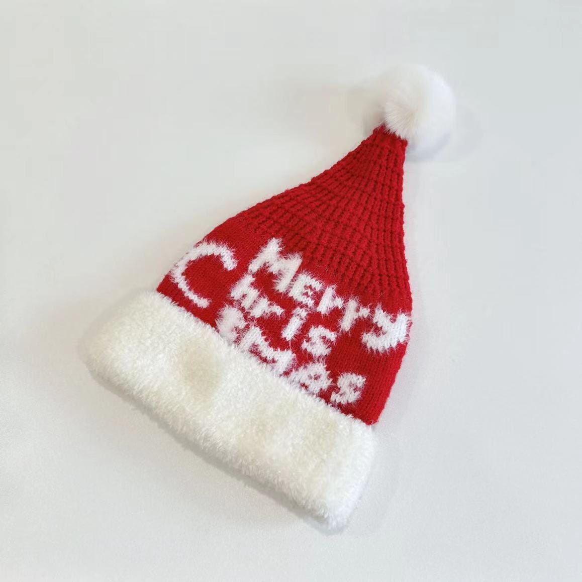 Czerwona, dzianinowa czapka Świętego Mikołaja z białym futrzanym obszyciem, napisem Merry Christmas i pomponem.