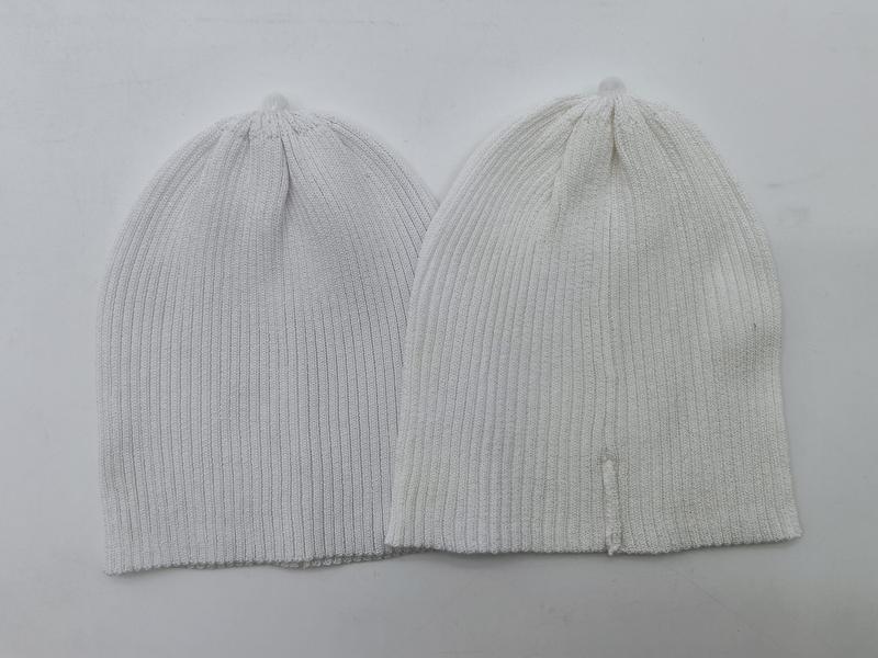 Dwie czapki beanie z prążkowanej dzianiny: jasnoszara i kremowa, ułożone płasko, widoczna tekstura i luźny krój.