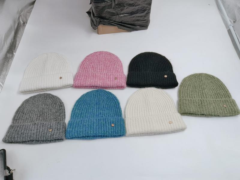 Siedem prążkowanych czapek beanie z podwiniętym mankietem w kolorach: biały, różowy, butelkowa zieleń, szałwia, szary, niebieski i kremowy.