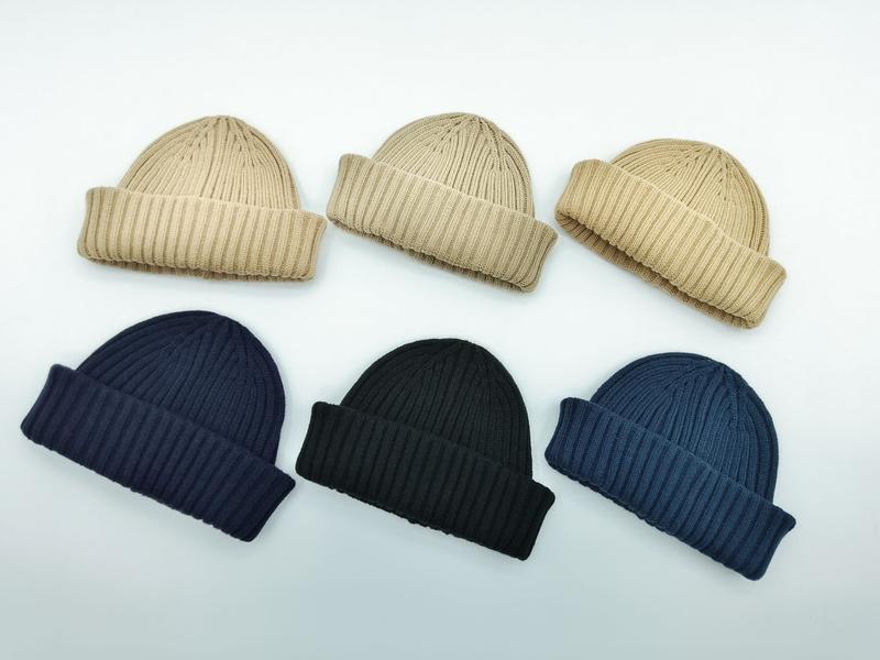 Sześć prążkowanych czapek beanie z podwiniętym mankietem w kolorach beżowym, granatowym, czarnym i stalowym błękicie.