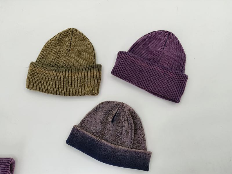 Trzy czapki beanie z prążkowanej dzianiny w kolorach oliwkowym, fioletowym i szaro-granatowym, ułożone płasko.