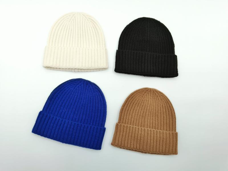 Cztery prążkowane czapki beanie z mankietem w kolorach: kremowym, czarnym, kobaltowym i wielbłądzim na białym tle.