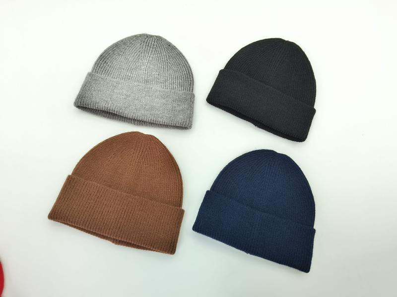 Cztery prążkowane czapki beanie z mankietem w kolorach: szarym, czarnym, brązowym i granatowym na białym tle.