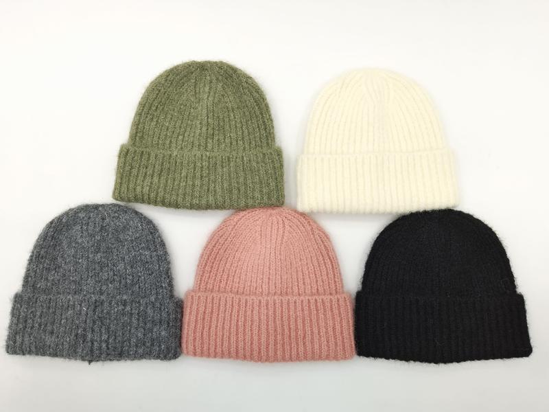 Pięć prążkowanych czapek beanie w kolorach: oliwkowym, kremowym, szarym, różowym i czarnym na białym tle.