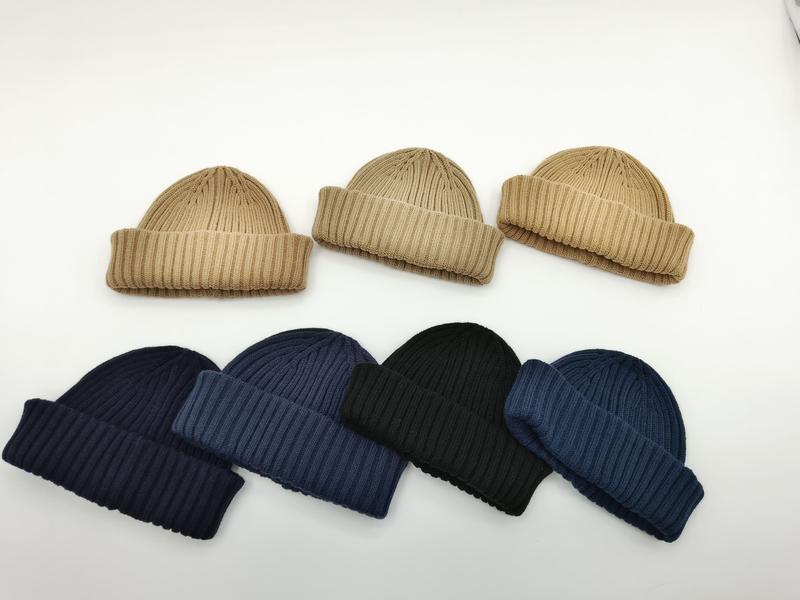 Siedem prążkowanych czapek beanie z mankietem w kolorach beżowym, granatowym, czarnym i niebieskim na białym tle.